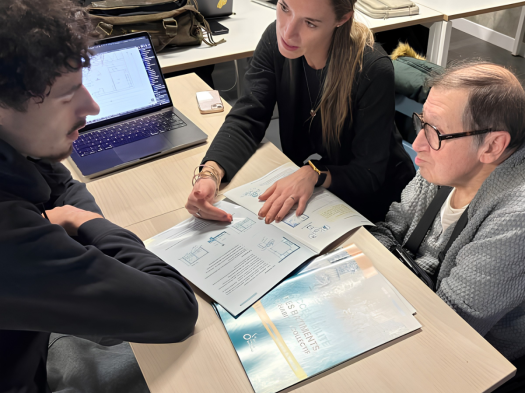 Trois personnes autour d'une table, l'une d'entre elles indique une brochure posée sur la table