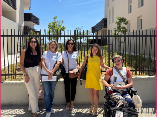 Cinq personnes sourient devant une grille, entre deux logements